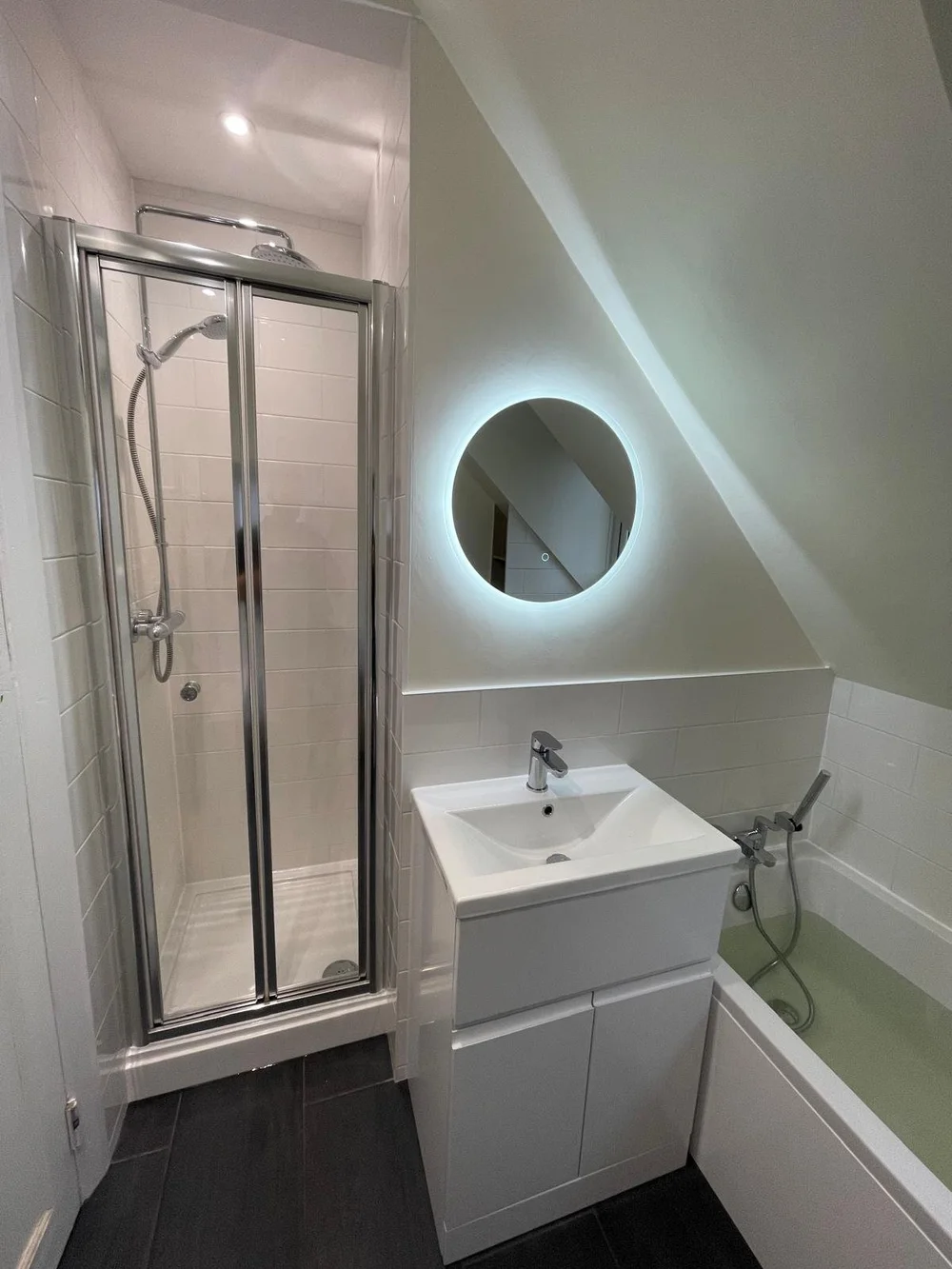 Compact loft shower room with backlit round mirror and bi-fold shower door — bathroom renovation Basingstoke