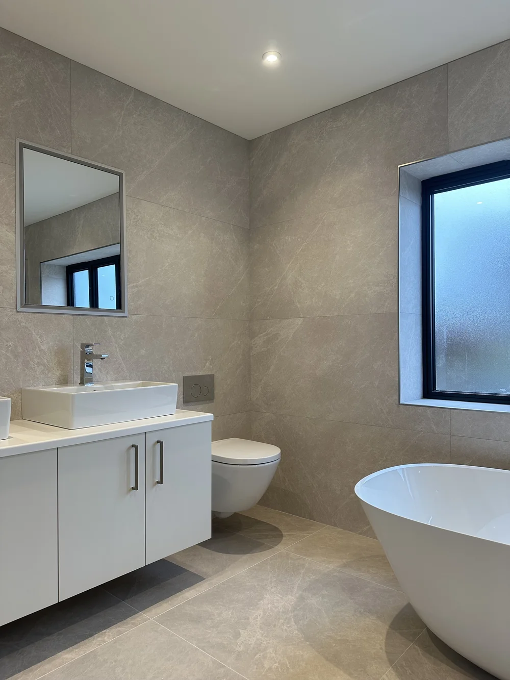 Contemporary stone-tiled bathroom with freestanding bath, floating vanity and twin basins — bathroom renovation Basingstoke
