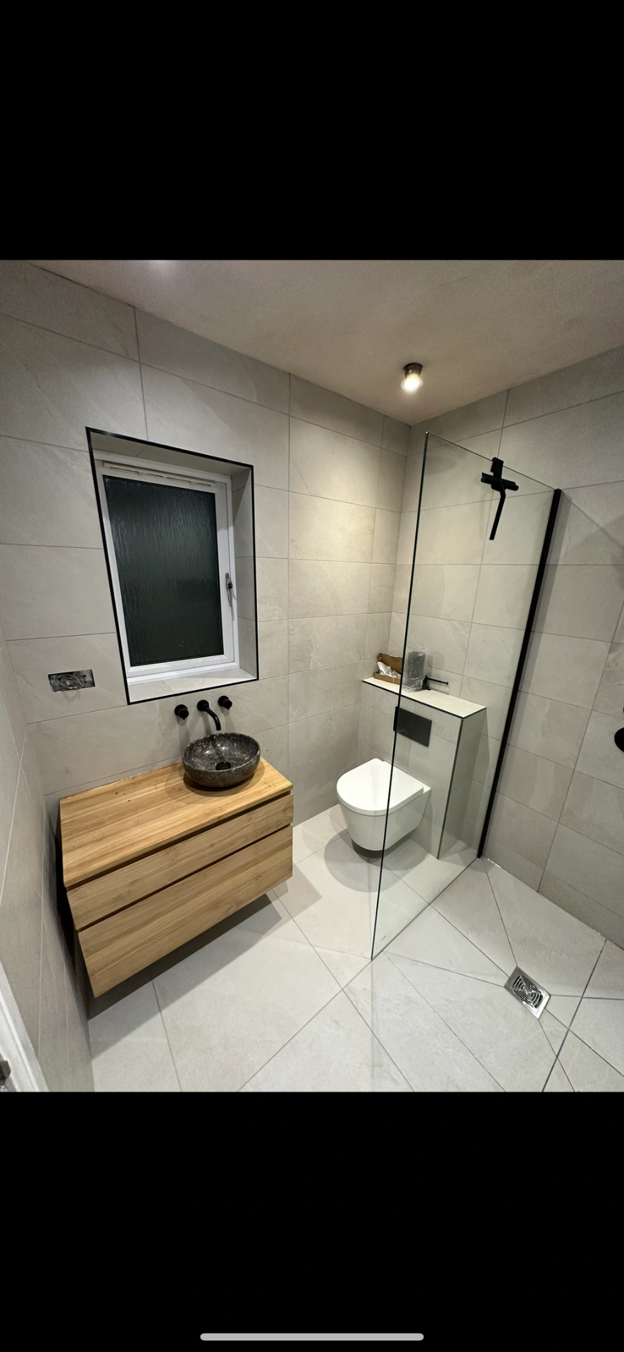 Wet room with oak floating vanity, stone vessel basin and black-framed walk-in shower — wet room installation Basingstoke