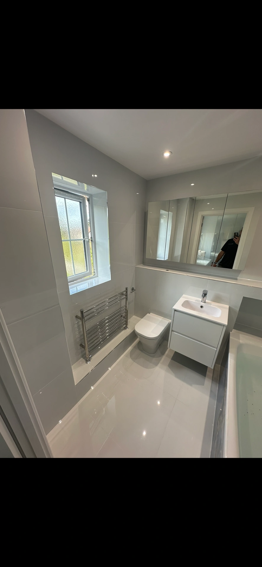 Bright white family bathroom with floating vanity, mirrored cabinet and gloss floor tiles — bathroom installation Basingstoke