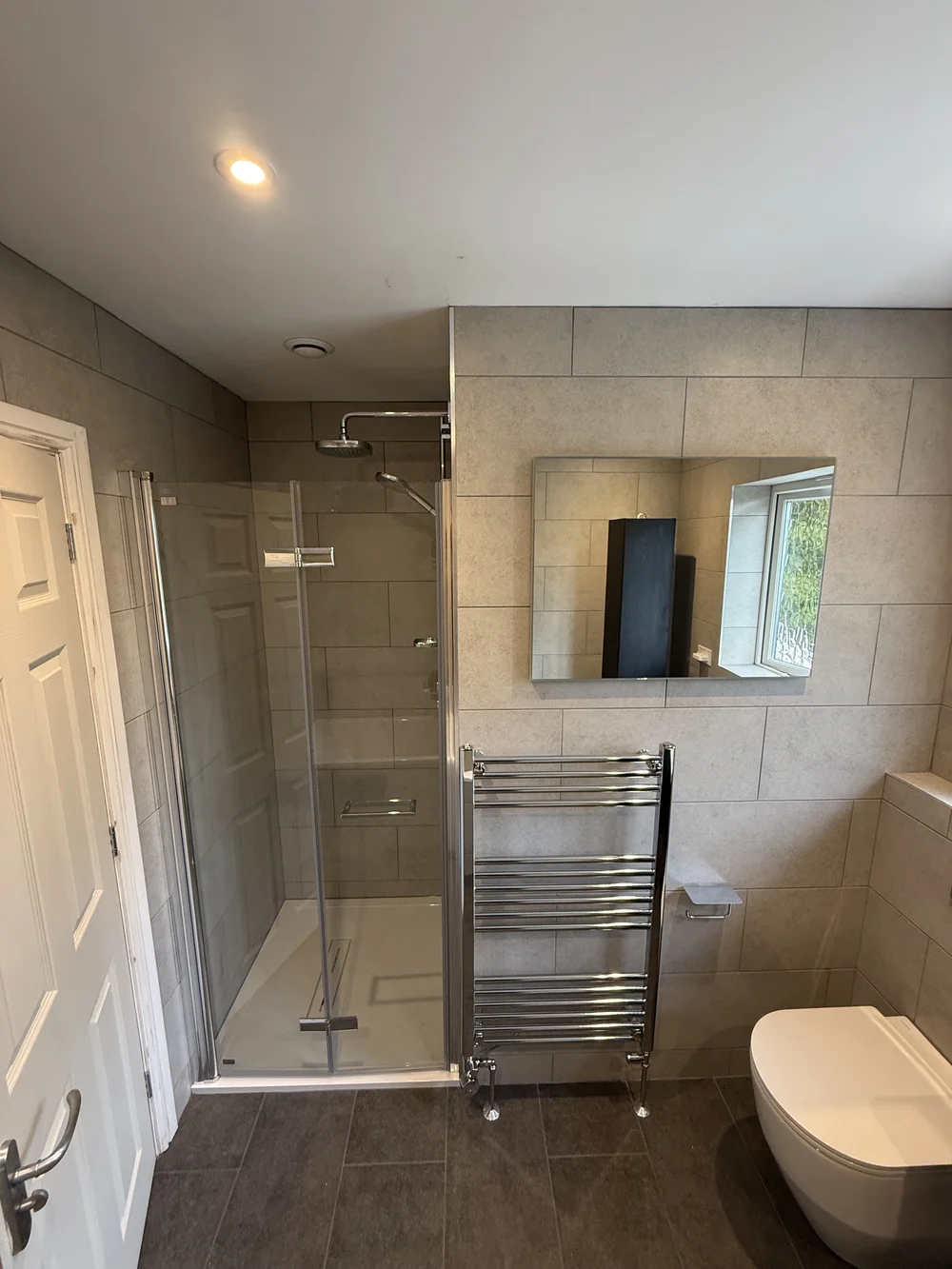 Stone-tiled family bathroom with hinged glass shower enclosure and chrome towel rail — bathroom installation Basingstoke