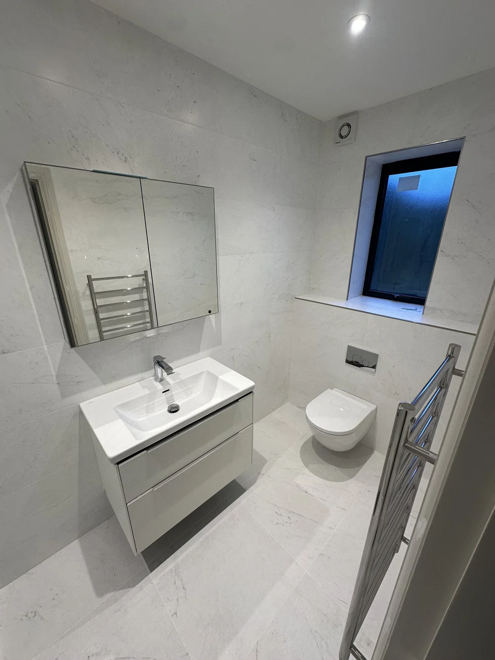 White marble ensuite with wall-hung vanity, mirrored cabinet and back-to-wall WC — Basingstoke