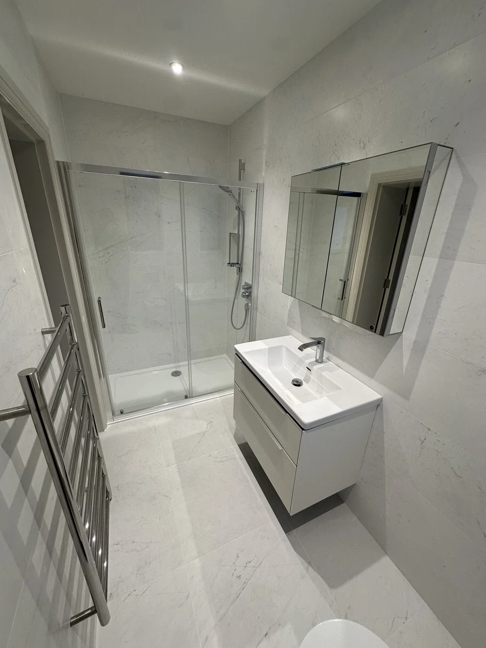 White marble shower room with sliding enclosure, wall-hung vanity and heated ladder rail — bathroom installation Basingstoke