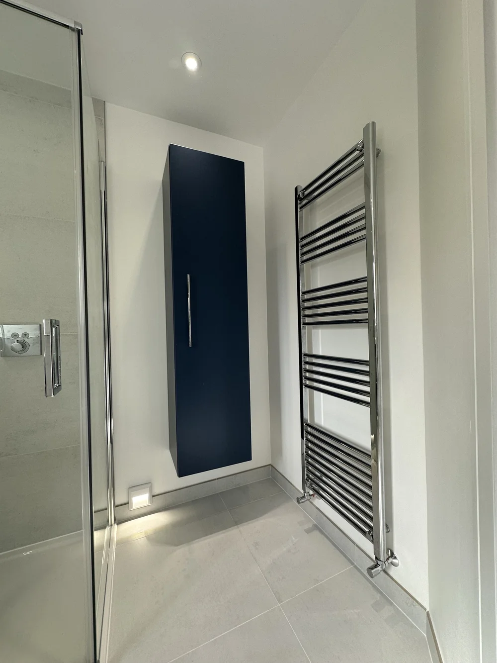Detail of navy wall-hung storage cabinet with chrome ladder radiator — bathroom design Basingstoke