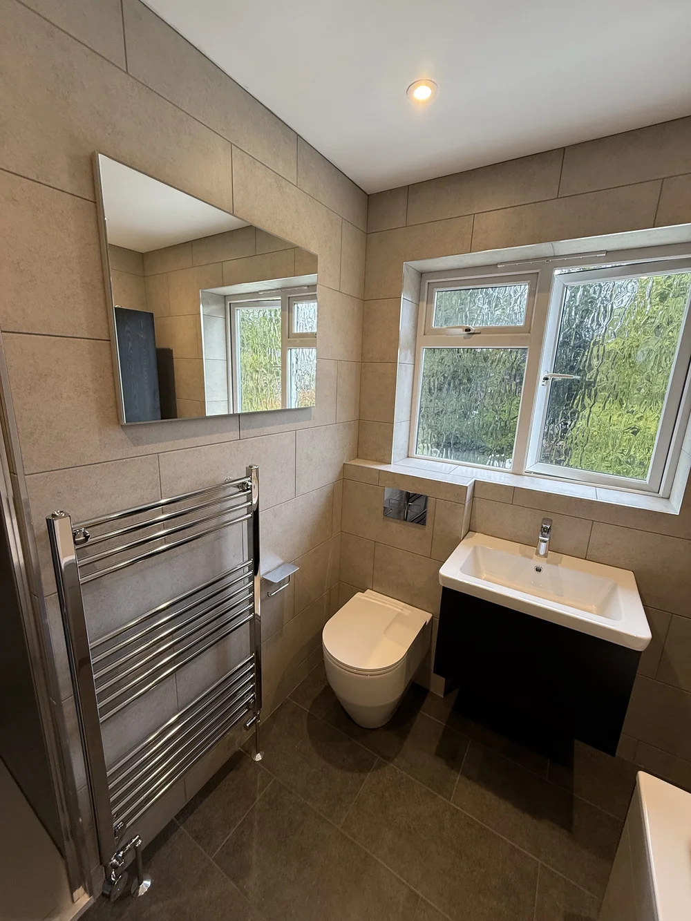 Beige-tiled bathroom with wall-hung black vanity and chrome heated rail — bathroom renovation Basingstoke