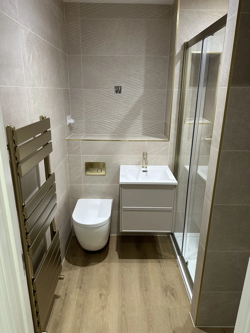 Textured stone shower room with brushed brass trim and designer towel rail — bathroom installation Basingstoke