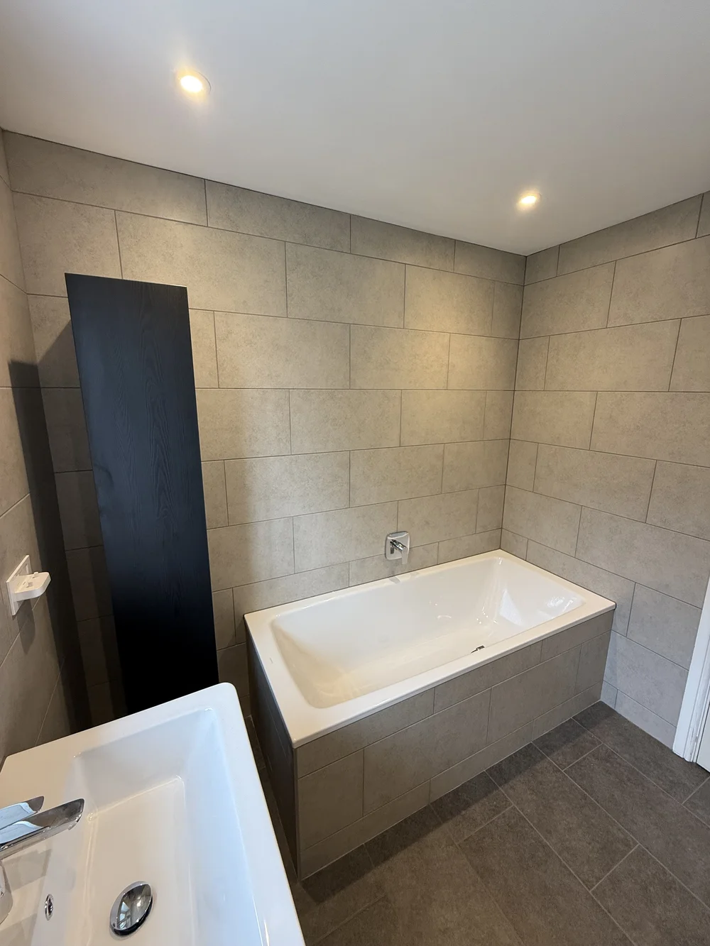Stone-tiled bathroom with panelled bath and tall black storage column — bathroom renovation Basingstoke