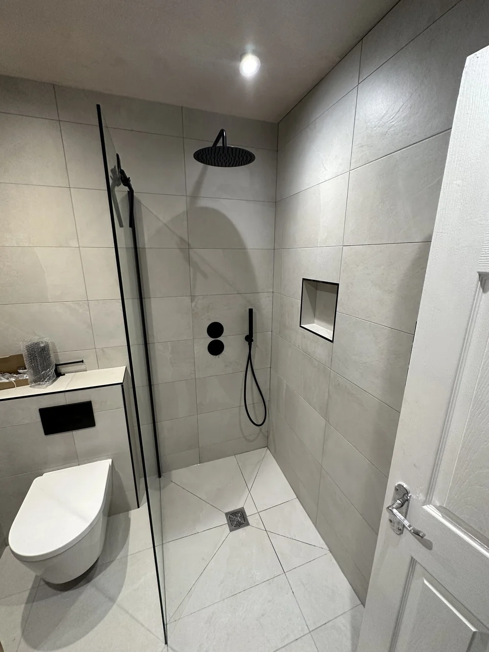 Stone-tiled walk-in shower with matte black rainfall head and recessed niche — wet room Basingstoke