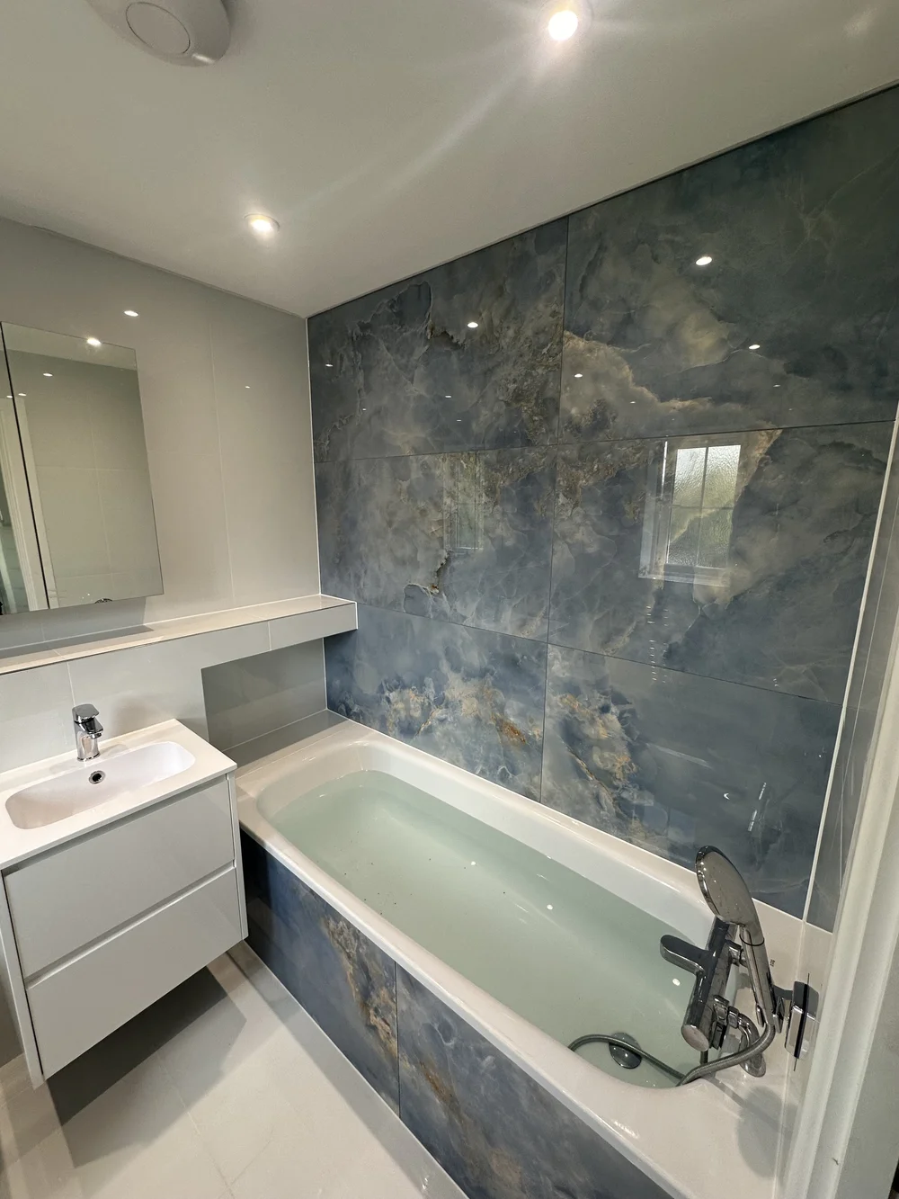 Family bathroom with blue onyx-effect feature wall, panelled bath and floating white vanity — bathroom installation Basingstoke
