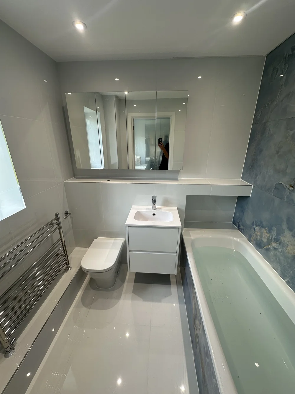 Bright family bathroom with mirrored cabinet, white vanity and blue onyx accent wall — bathroom renovation Basingstoke