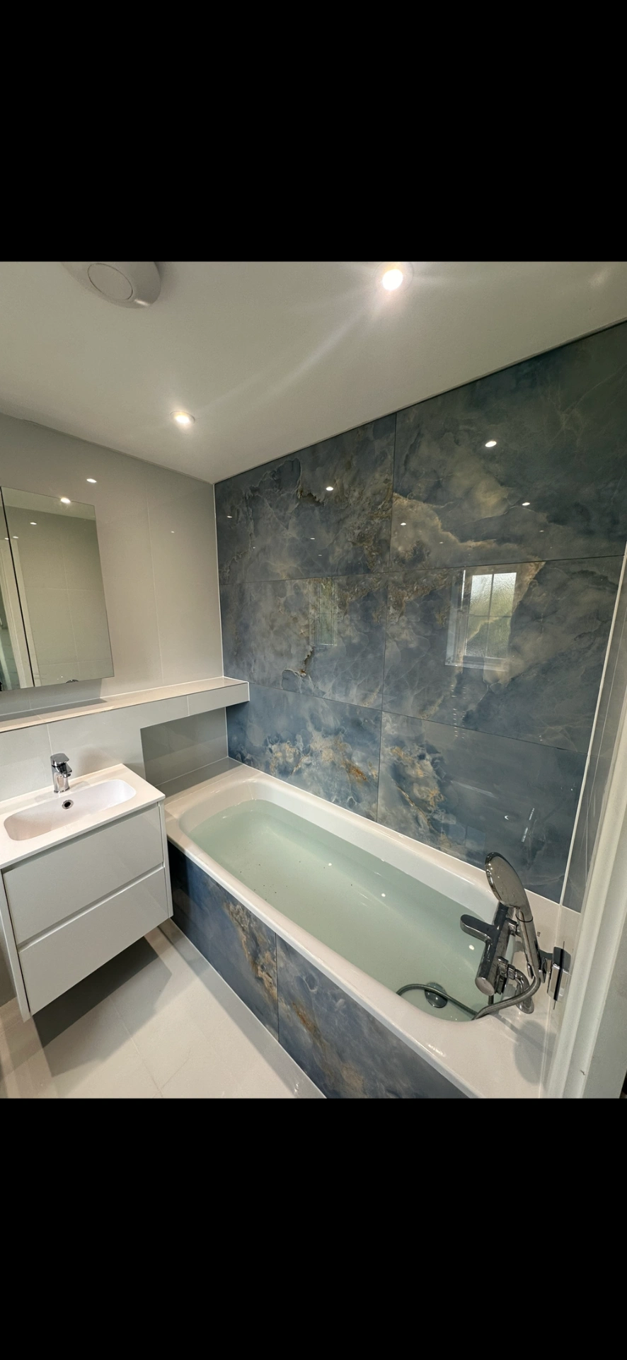 Bathroom with blue onyx-effect feature wall, panelled bath and floating white vanity — bathroom renovation Basingstoke