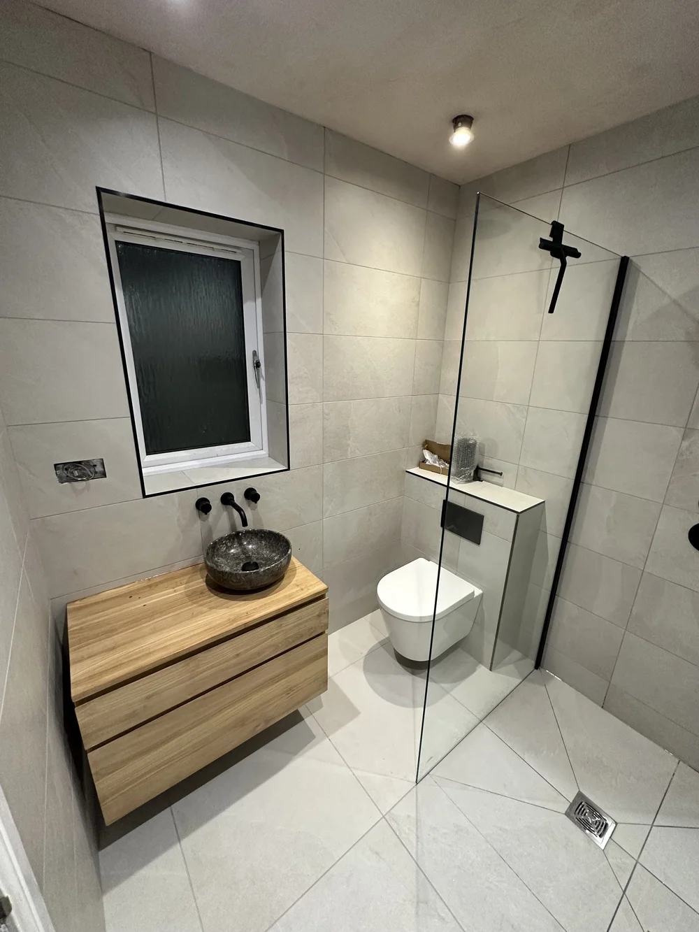 Wet room with oak floating vanity, stone basin and glass walk-in screen — wet room installation Basingstoke