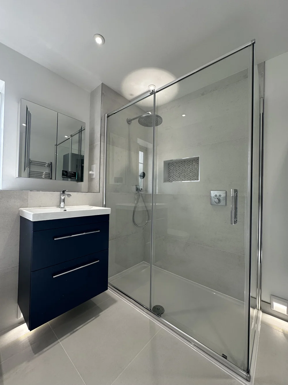 Modern ensuite with navy floating vanity, mirrored cabinet and sliding-door shower enclosure — bathroom installation Basingstoke