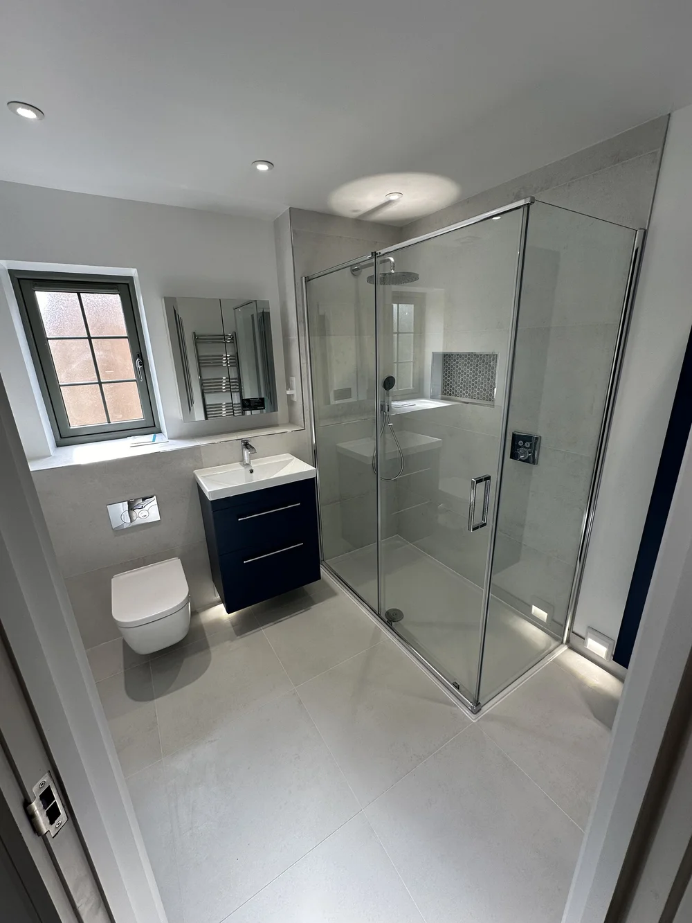 Fitted ensuite with navy vanity, wall-hung WC and corner shower enclosure — bathroom installation Basingstoke