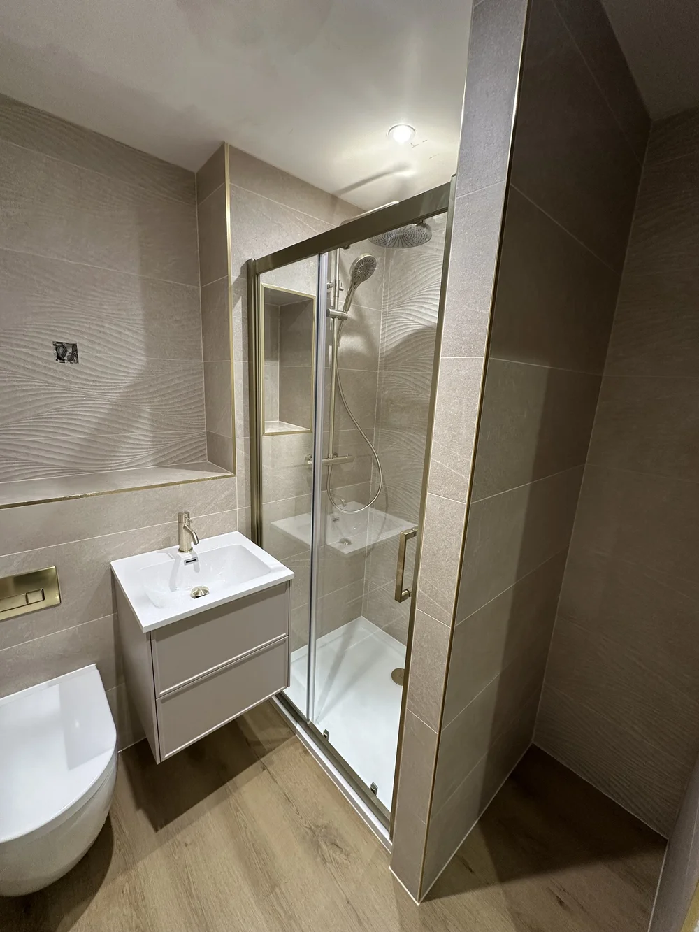 Wave-tiled shower room with brushed brass fittings and oak-effect floor — bathroom renovation Basingstoke