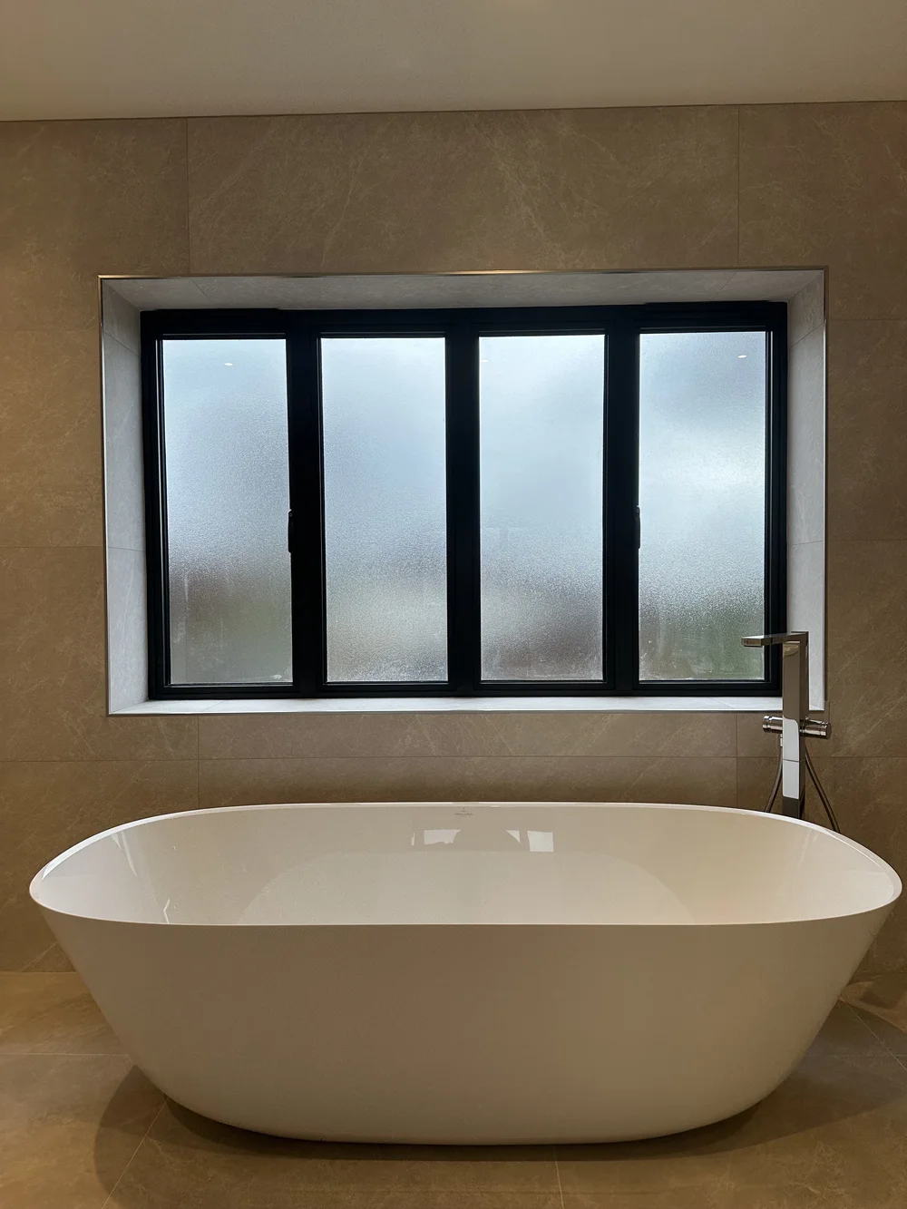 Freestanding stone-resin bath under crittall window in marble master bathroom — bathroom installation Basingstoke